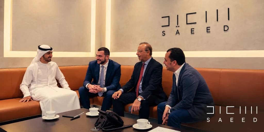 Four colleagues in conversation on orange sofas in a SAEED meeting room, with the Saeed wordmark on the wall
